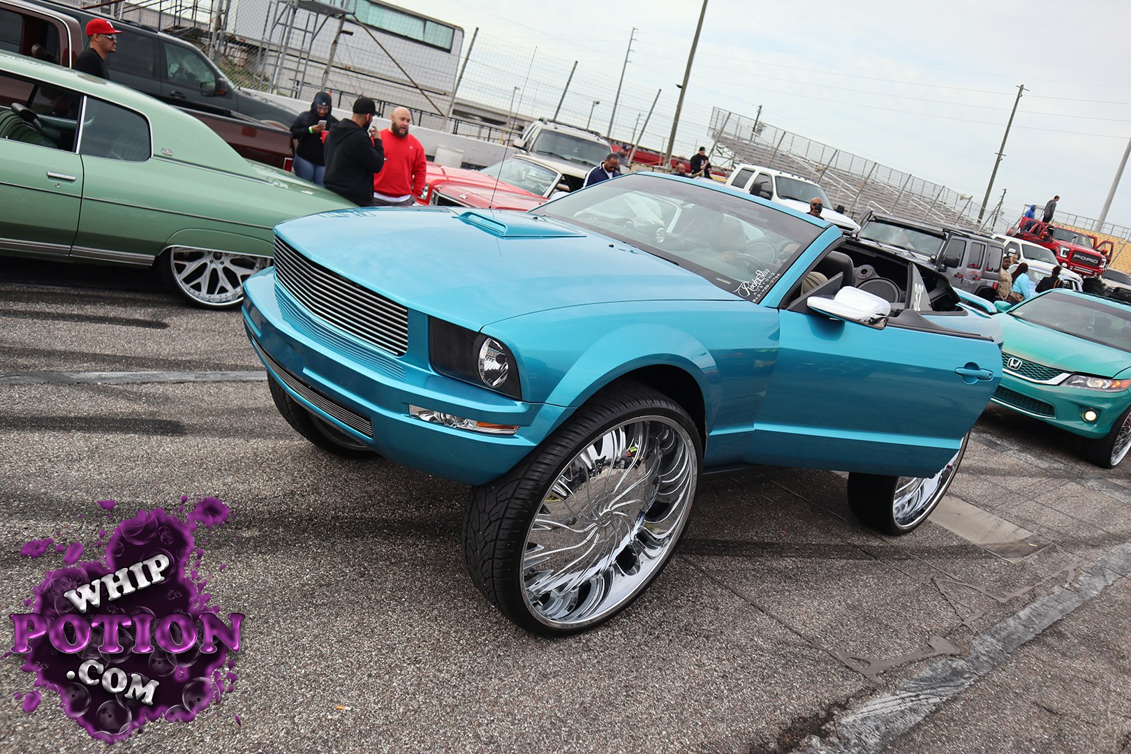 This custom blue Mustang convertible sits on massive chrome rims with a clean, high-gloss finish and a full aftermarket grille treatment that gives the nose a sharp, billet look. The body stays smooth and simple, letting the oversized wheels and open-top street-car stance do the talking while the light interior keeps the build looking crisp.