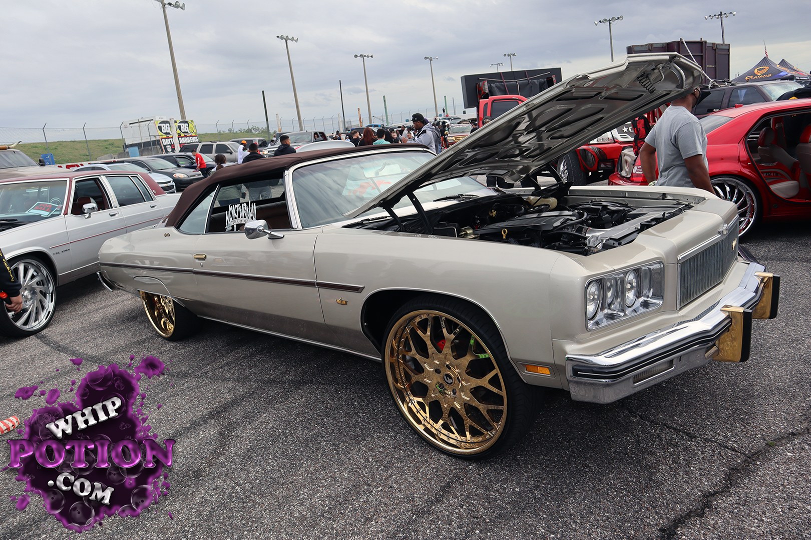 This big-body classic Chevy convertible is laid out with a clean two-tone finish, a brown soft top, and massive gold multi-spoke wheels tucked under the fenders. The hood’s propped open to show off the bay, while the chrome bumpers, stacked headlights, and long slab-sided profile give it that unmistakable full-size cruiser attitude.