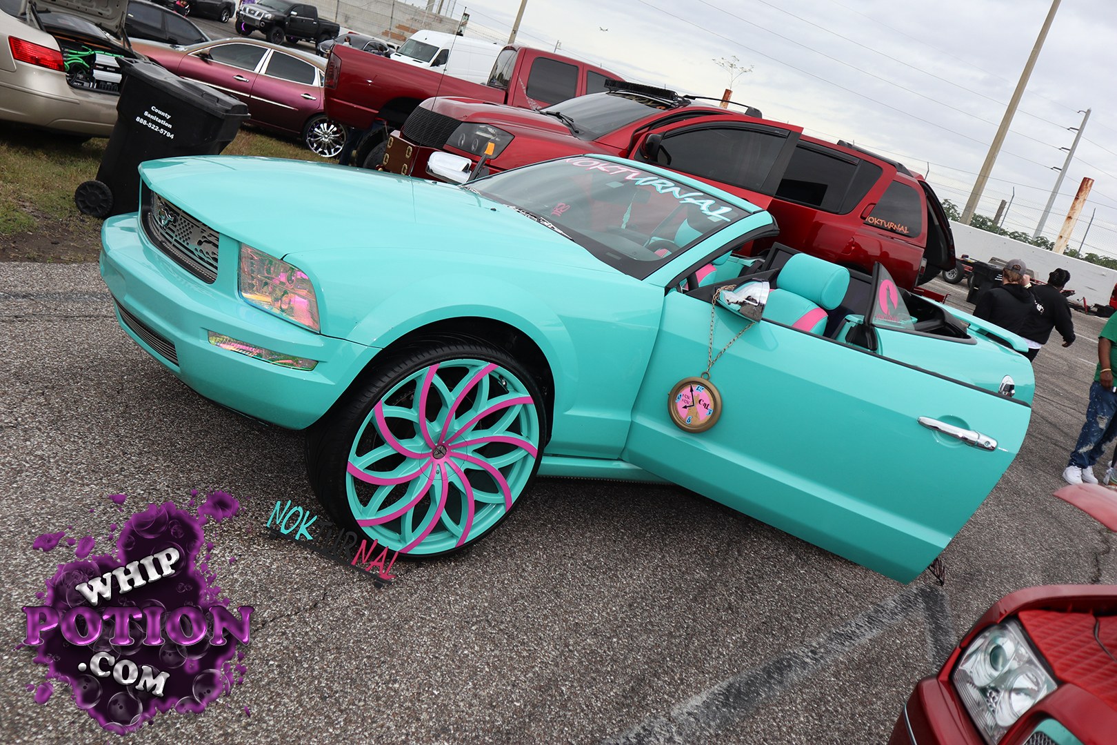 A mint-turquoise Chrysler 300C convertible sets the tone with a clean custom drop, color-matched interior, and wild pink-and-teal multi-spoke wheels. The shaved, smooth bodywork and club-style windshield banner give it a polished show-car vibe, while the open cabin and big wheel package lean hard into full custom culture without losing the luxury-sedan roots.