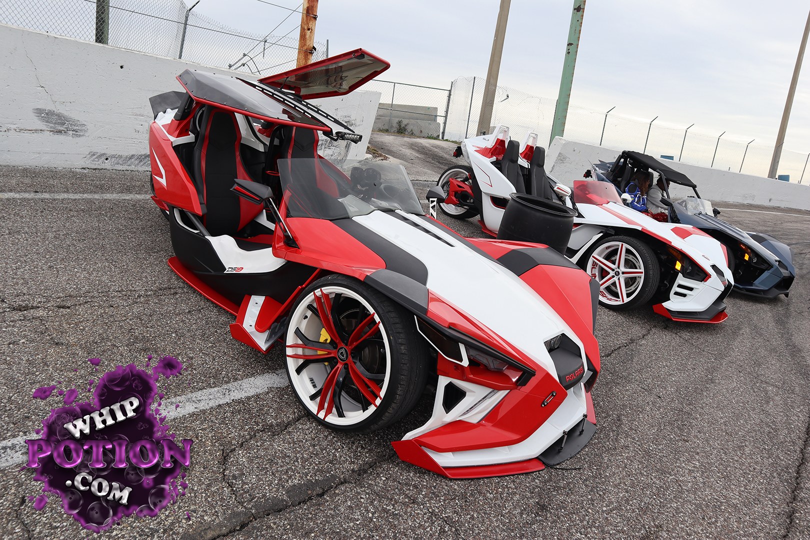 Three Polaris Slingshots line up in wild custom trim, with the lead machine going all-in on a red, white, and black scheme, sharp aero pieces, and a dramatic roof setup. Big-diameter custom wheels, low-slung bodywork, and the open cockpit layout give the whole group a slammed, show-ready look that fits the Slingshot’s street-machine personality perfectly.