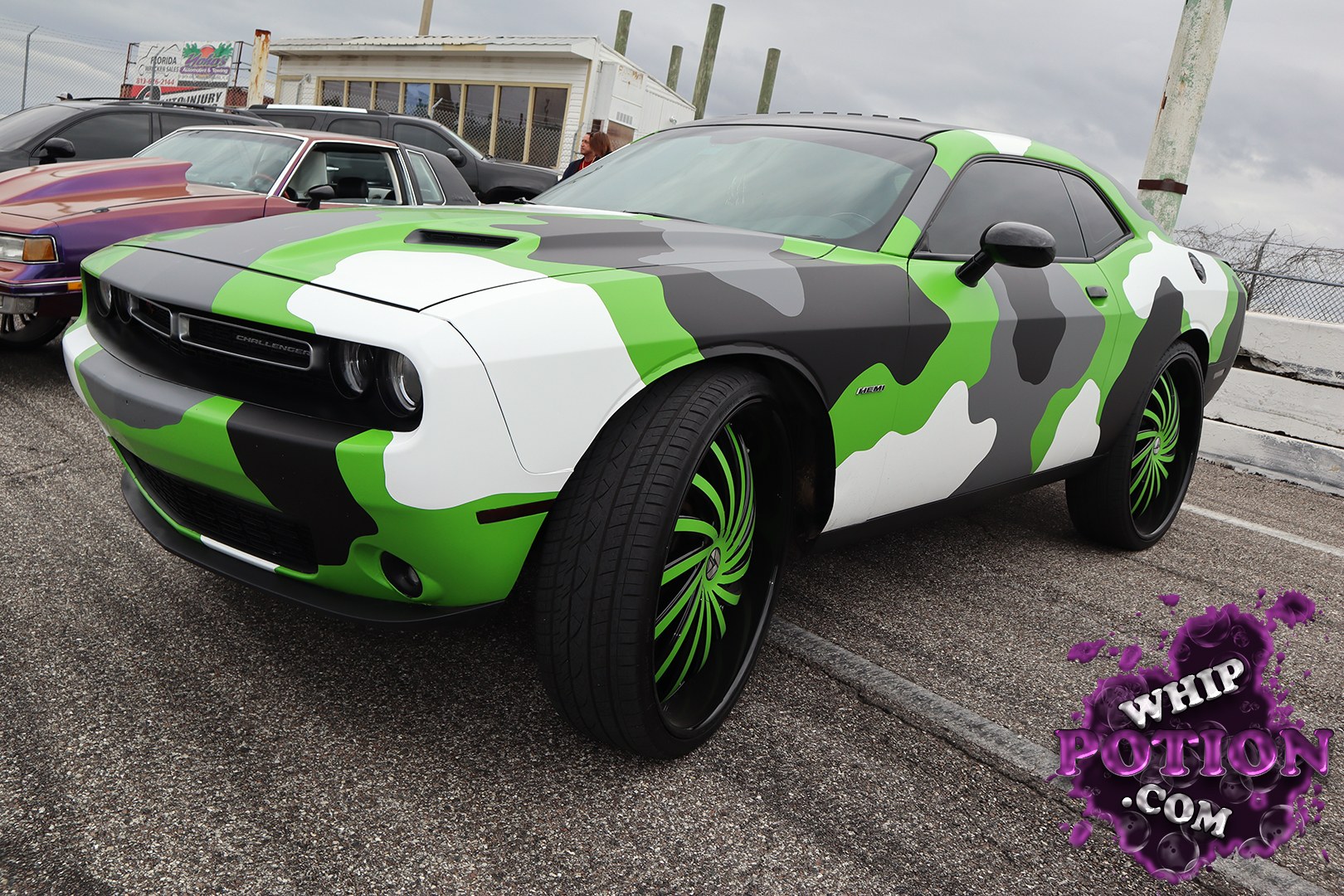 This Dodge Challenger goes full custom with a wild green, gray, black, and white camouflage wrap, plus oversized green-accented wheels that give it a real street-machine attitude. The long coupe body, shaker-style hood scoop, and dark tinted glass keep the look tough, while the stance sits just right without trying to fake a lowrider vibe.